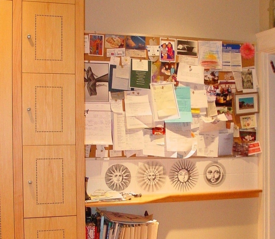 A cluttered bulletin board by custom kitchen cabinetry.